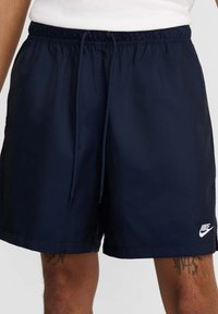 Granatowe szorty kąpielowe wykonane z lekkiego materiału, z elastycznym ściągaczem w pasie oraz małym białym logo Nike na dole.