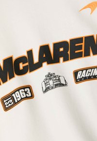 Sudadera blanca con el logo de "McLaren" en negro y naranja, incluye una ilustración de un coche de carreras y el año de fundación "1963".