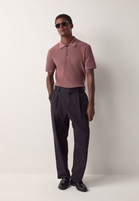 Kortere mouw, geribbelde bordeaux polo met drieknopensluiting, gecombineerd met zwarte, hoge taille broek en zwarte schoenen, gedragen met een zonnebril.