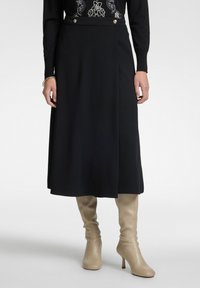 Gonna nera di lunghezza al ginocchio con uno spacco laterale, caratterizzata da due bottoni dorati in vita. Abbinata a stivali beige con tacco alti fino al ginocchio.