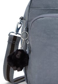Sac en tissu gris avec une finition texturée, doté d'un clip en métal, d'une bandoulière rayée et d'un porte-clé gorille noir attaché.
