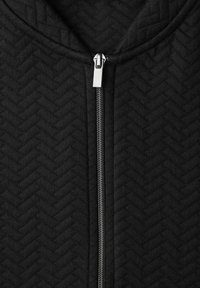 Zwarte jas met ritssluiting, voorzien van een visgraatstructuur en zilverkleurige ritsdetails. Gladde stof met een gestructureerd ontwerp en een hoge kraag.