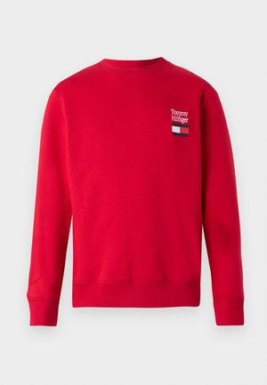 Rdeča trenirka s krožnim izrezom, z ribastimi manšetami in robom. Ima vezeno "Tommy Hilfiger" logotip in zastavni simbol na prsih.