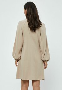 Abito beige a maniche lunghe con una vestibilità comoda e maniche a sbuffo, caratterizzato da una texture liscia e una lunghezza a metà coscia.