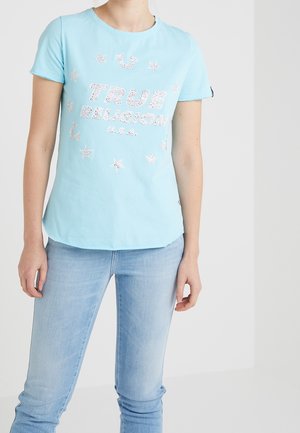 Osoba ubrana w jasnoniebieską koszulkę True Religion z motywami gwiazdy i podkowy, w połączeniu z jasnoniebieskimi jeansami.