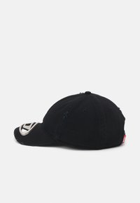 Svart baseballcap med buet visir, slitt tekstur, s�ølvfarget logo på fronten og en liten rød label på siden.