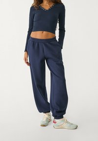 Marineblaue Langarm-Crop-Top mit Knopf-Akzenten und dazu passenden übergroßen Jogginghosen. Der Stoff scheint weich zu sein; die Hosen haben elastische Bündchen und einen elastischen Bund.