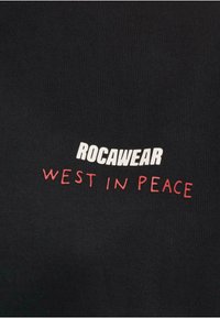 Juodas medvilninis marškinėlis su „ROCAWEAR“ ryškiu baltu šriftu ir „WEST IN PEACE“ raudonu užrašu, išdėstytu per krūtinę.