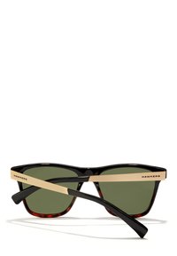 Black and gold Hawkers sunglasses with dark green lenses, rectangular frame, and one temple crossed over the other on a white background.