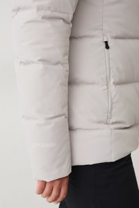 Lichtgrijze pufferjack met een gestikt ontwerp, voorzien van een ritszak aan de zijkant en kleine witte tekst op de mouw.