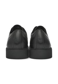 Scarpe in pelle nera con finitura liscia, punta rotonda, profilo basso e suola in gomma testurizzata con tacco leggero. Vista posteriore mostrata.