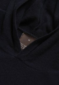 Ciemnoniebieska bluza z kapturem wykonana z miękkiego materiału, z dekoltem w serek. Posiada brązową metkę wewnątrz z oznaczeniem rozmiaru "M". Gładka tekstura, minimalne detale.