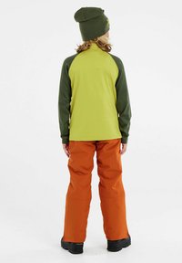 Langsleeve shirt met groene mouwen en een lichtgroen lichaam, gecombineerd met oranje wijde broeken. Draagt een groene gebreide beanie.