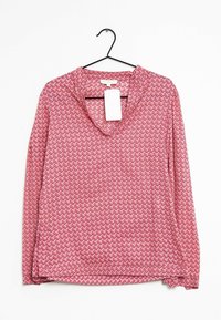 Langärmlige Bluse in Pink mit einem geometrischen Zickzackmuster, leichtem Stoff, V-Ausschnitt und einem Etikett, das an einem Kleiderbügel hängt.