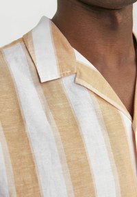 Korte mouwen shirt in beige en witte strepen, gemaakt van lichte stof. Heeft een puntige kraag en zichtbare stikseldetails.