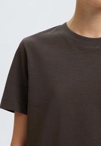 Hnedé bavlnené tričko s krátkymi rukávmi a okrúhlym výstrihom. Vyznačuje sa hladkou textúrou a minimalistickým dizajnom bez ďalších vzorov alebo akcentov.