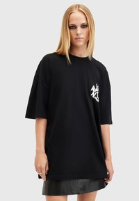 Černé oversized bavlněné tričko s krátkými rukávy a bílým grafickým logem na levé hrudi. Jednoduchý, volný střih.