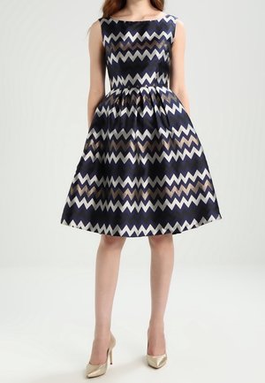 Robe bleu marine avec un motif en zigzag crème et cuivre. Sans manches, corsage ajusté menant à une jupe bustier évasée à hauteur des genoux.
