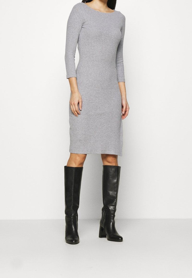 Robe grise à côtes avec un décolleté bateau, des manches trois-quarts et une silhouette ajustée. Associée à des bottes en cuir noires jusqu'aux genoux.