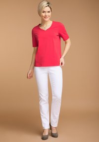 Top rosso a maniche corte con scollo a V e dettagli a bottoni, abbinato a pantaloni bianchi aderenti e tacchi alti grigi. Tessuto morbido e design aderente.