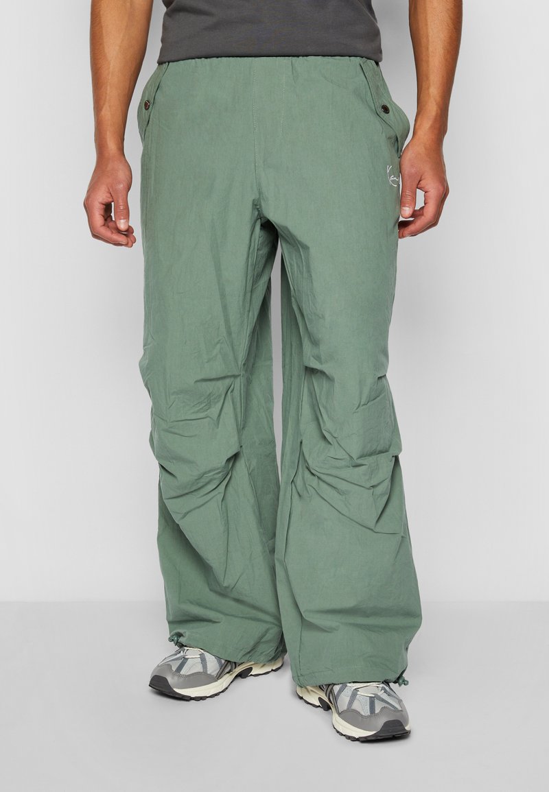 Pantalons d'extérieur vert clair à coupe décontractée, avec une taille élastique, des poches et une texture ripstop. Associés à des chaussures de randonnée grises.