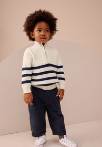 Maglione a righe bianche con strisce blu navy, collo con mezza zip e texture a coste, abbinato a pantaloni blu scuro e sneakers bianche.