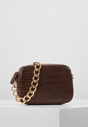 Ciemnobrązowa prostokątna torba na ramię o fakturze krokodyla z grubym złotym łańcuchem jako paskiem, położona na białej powierzchni.