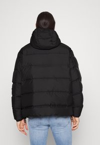 Giacca puffer nera con cappuccio, caratterizzata da un design trapuntato e orlo elasticizzato. Texture liscia e stile minimalista.