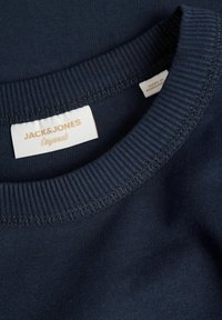 Ναυτικό μπλε βαμβακερό T-shirt με ριμπ λαιμόκοψη. Διαθέτει ετικέτα υφάσματος με χρυσό κείμενο που γράφει "JACK&JONES Originals." Λείος υφασμάτινος χαρακτήρας.