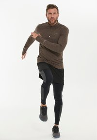 Brun langærmet træningsskjorte med lynlås, parret med sorte shorts og tætsiddende sorte leggins med tekstureret detaljer og grå paneler.