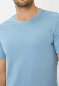 Lysblå bomulds T-shirt med rund hals og korte ærmer. Blød tekstur, tætsiddende design og standard syninger langs halsudskæringen og ærmerne.