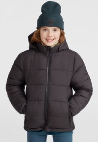 Svart puffermantel med huva, med dragkedja framtill och vadderad design. Bärs med en mörkgrön ribbad mössa och under en ljus skjorta.