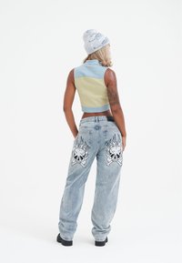 Skuren tvåfärgad väst i ljusblått och gult, i kombination med löst sittande ljusblå jeans med stora dödskalle- och flammgrafik.