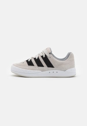 Light gray suede sneaker with black stripes, white rubber sole, textured lateral accents, and flat laces, designed for casual wear.