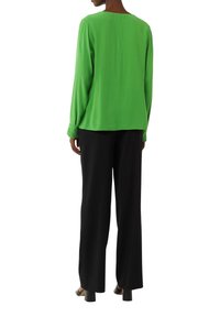 Green long-sleeve blouse with a relaxed fit, round neckline, and flowing fabric, paired with black wide-leg trousers and heeled shoes.
