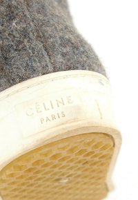 Gros plan sur le talon d'une basket en laine grise avec une semelle en caoutchouc blanc montrant le logo "CELINE PARIS" ainsi qu'une semelle extérieure jaune texturée.