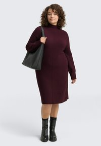 Burgunderfarbenes Strickkleid mit hohem Kragen und langen Ärmeln, das eine schmale Passform aufweist. Kombiniert mit einer schwarzen Lederhandtasche und klobigen schwarzen Stiefeln.