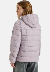Vaaleanlila puffer-takki, jossa on huppu, ja joka sisältää pystysuoria tikkausosuuksia sekä joustavat hihansuut. Pehmeä ja sileä texture.