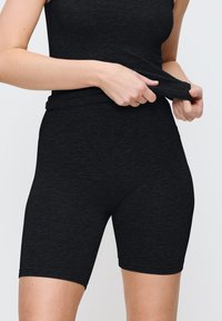 Svarta stretchtygshorts med en slät textur, med en hög midja och längd till mitten av låret, som erbjuder en figurnära silhuett.
