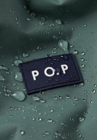 Groen waterdicht materiaal met zichtbare waterdruppels, voorzien van een donkerblauwe rechthoekige patch met de inscriptie "P.O.P" in witte letters.