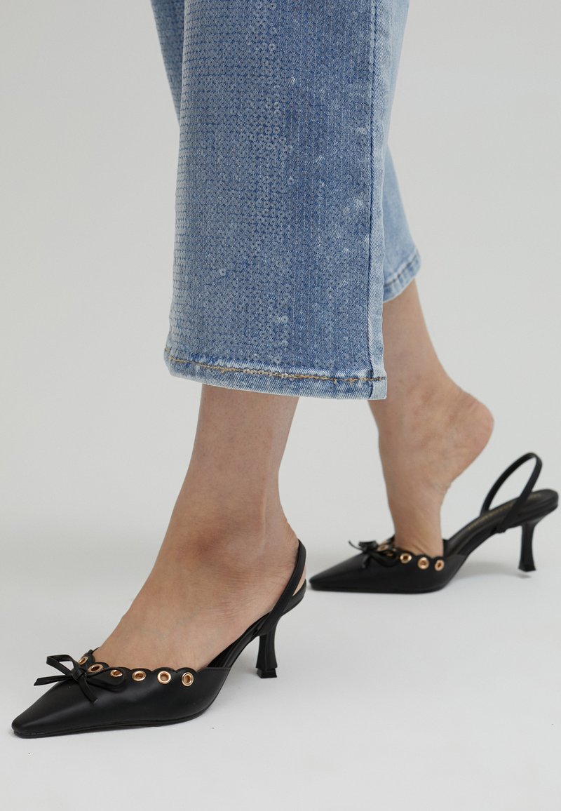 Svarta slingback-klackar med spetsiga tår, guldögon accenter och en frontbåge detaljer. Bärs med ljusblå cropped-jeans.