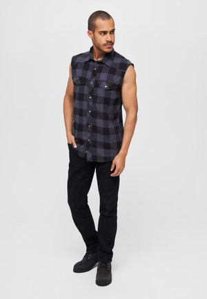 Chemise en flanelle à manches courtes à carreaux noirs et gris, avec deux poches avant et fermeture à boutons. Associée à un jean noir et des bottes.
