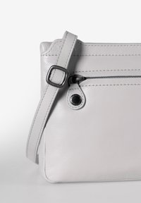 Graue Lederhandtasche mit flachem Design, ausgestattet mit einer Reißverschluss-Vordertasche, strukturiertem Oberflächenmaterial und einem verstellbaren Riemen mit einer Metallniete.