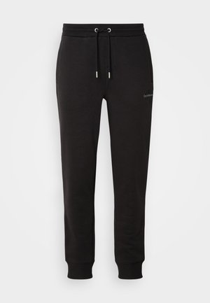 I pantaloni di felpa neri in cotone presentano una vita elasticizzata con cordino, tasche laterali e polsini a coste, progettati per conforto e funzionalità.