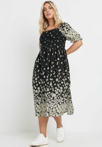 Svart blommig klänning med smockad midja, korta puffärmar och en flödande kjol prydd med vita och gula prästkragar. Bärs med vita sneakers.