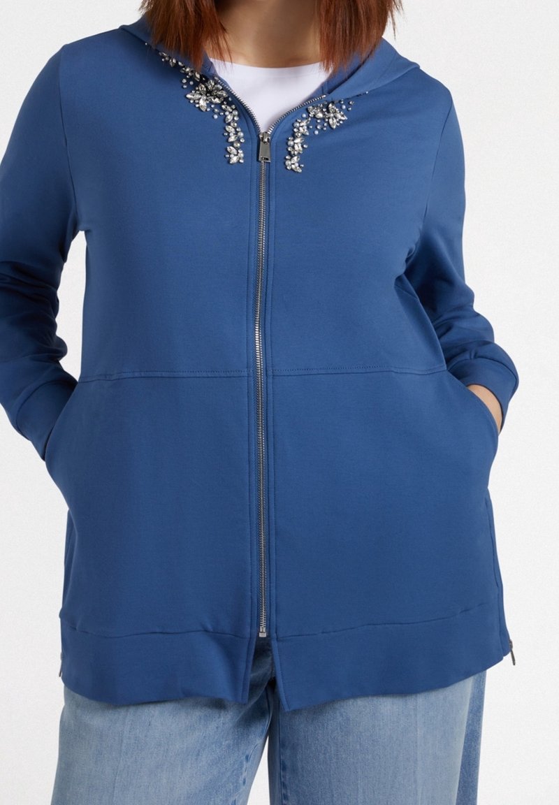 Blue zip-up hoodie with embellished neckline, soft cotton blend material, two front pockets, and a relaxed fit.