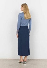 Dlhá námornícka sukňa s priliehavým modrým topom. Rukávy majú čipkový detail. Modelka má na sebe strieborné muly na podpätku. Hladká textúra látky.