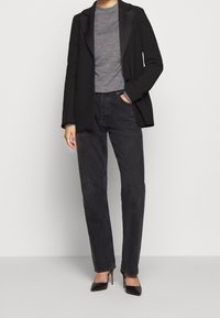 Schwarzes Blazer mit Satinrevers, graues, figurbetontes T-Shirt, schwarze gerade geschnittene Jeans und schwarze spitze Pumps. Glatte Texturen und minimalistisches Design.