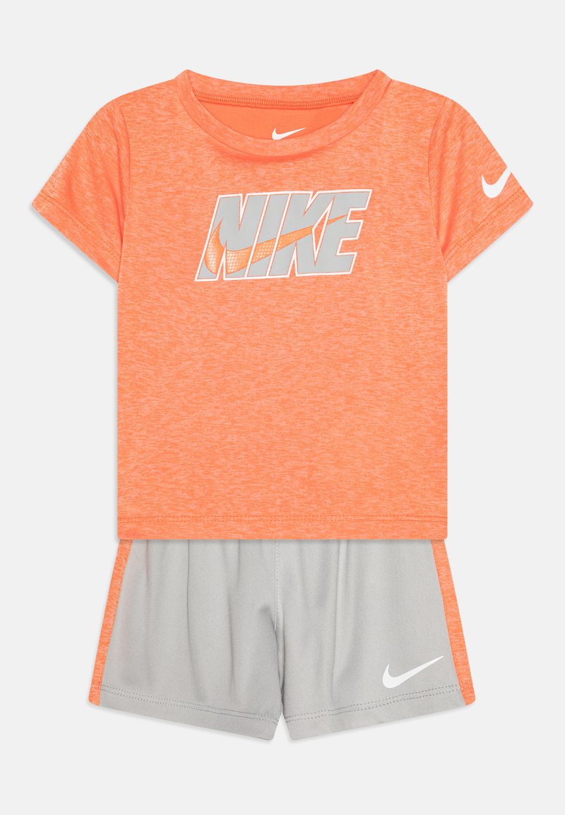 Oranžinis Nike trumpas rankovės marškinėlis su pilku logotipu, derinamas su pilkomis šortais, turinčiais baltą akcentą ir logotipą. Minkšta, lengva medžiaga.