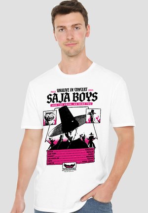Young man wearing a white T-shirt with a black and pink graphic promoting a 2025 concert tour by Saja Boys featuring stylized figures and city names.